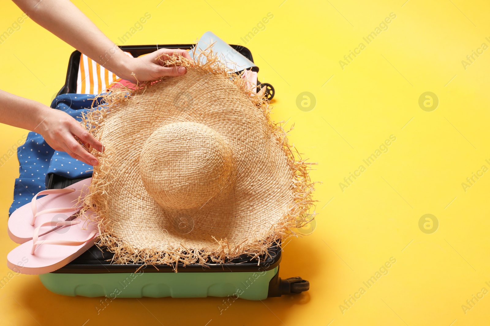 Photo of Woman packing suitcase on yellow background, closeup. Space for text