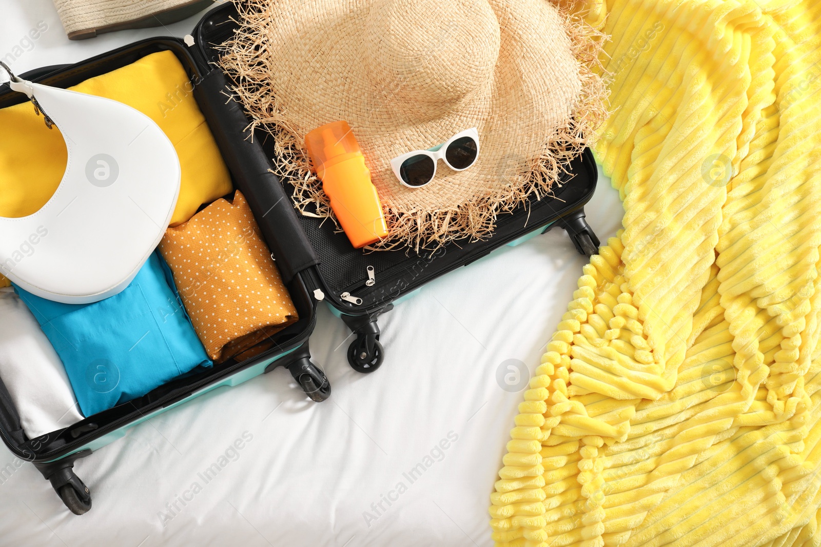 Photo of Open suitcase with traveler's belongings on bed, top view