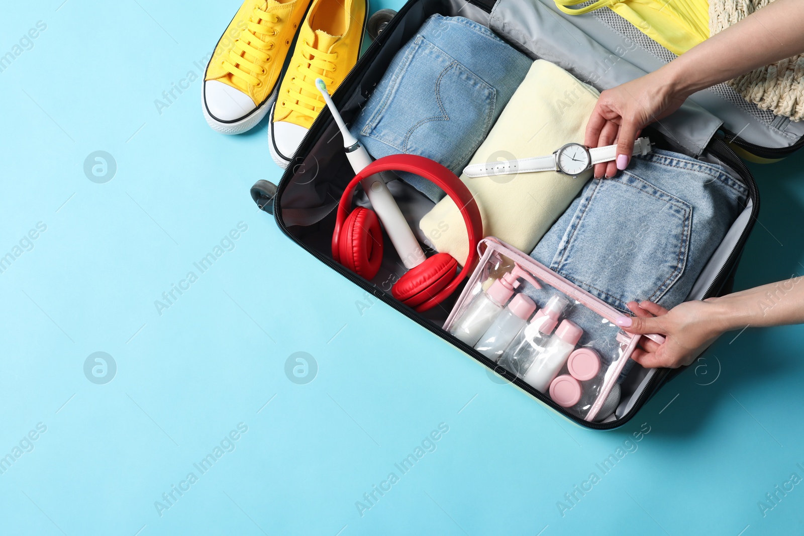 Photo of Woman packing suitcase on light blue background, top view. Space for text