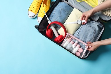 Photo of Woman packing suitcase on light blue background, top view. Space for text