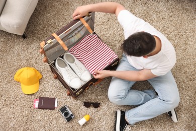 Photo of Man packing suitcase on floor at home, top view