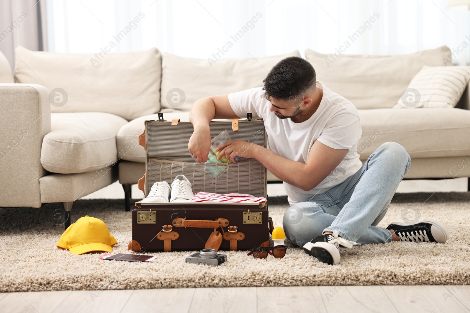 Photo of Man packing suitcase on floor at home