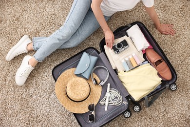 Woman packing suitcase for trip on floor indoors, top view