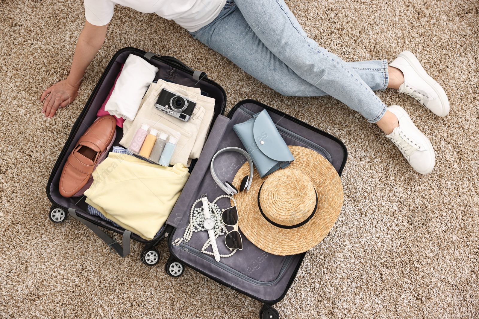 Photo of Woman packing suitcase for trip on floor indoors, top view