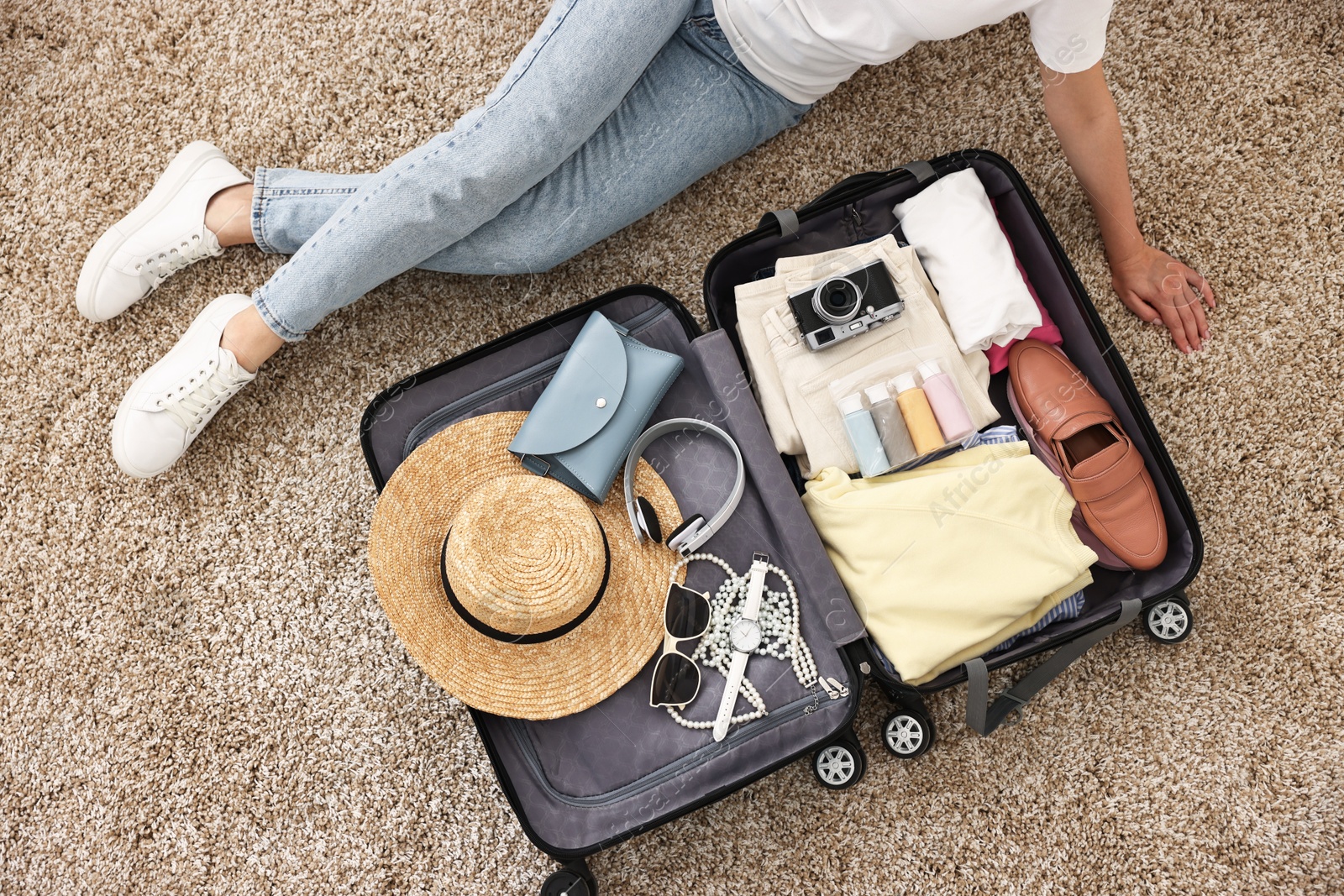 Photo of Woman packing suitcase for trip on floor indoors, top view