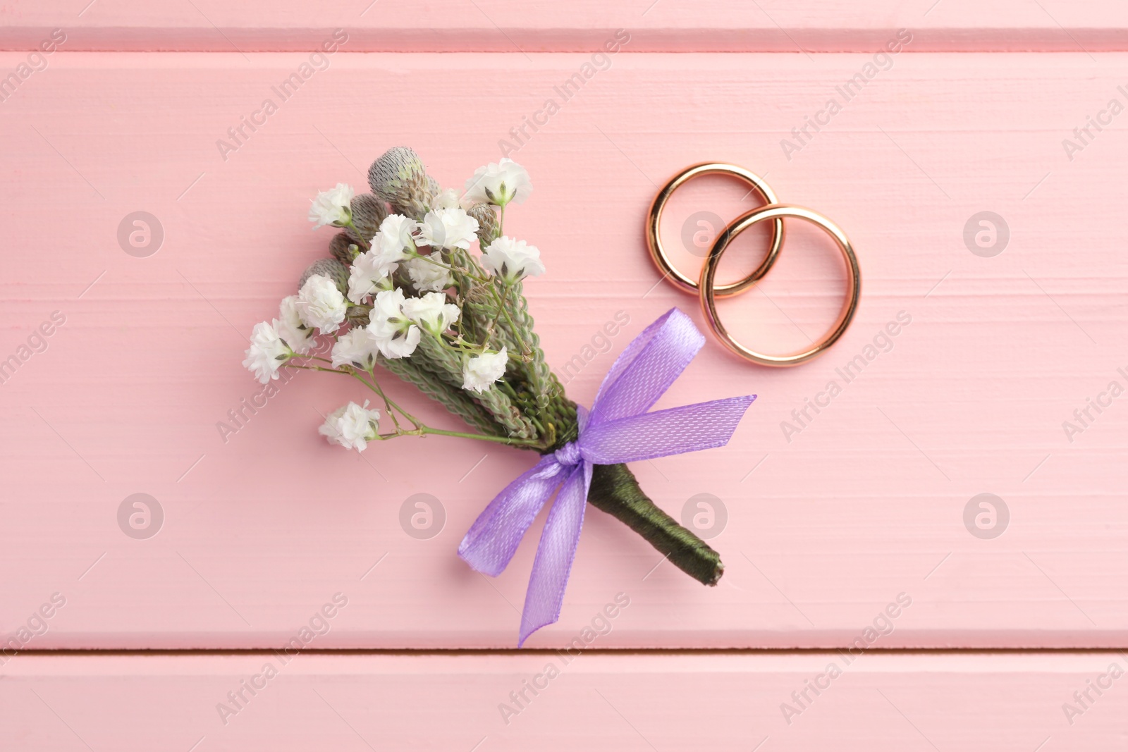 Photo of Small stylish boutonniere and rings on pink wooden table, flat lay