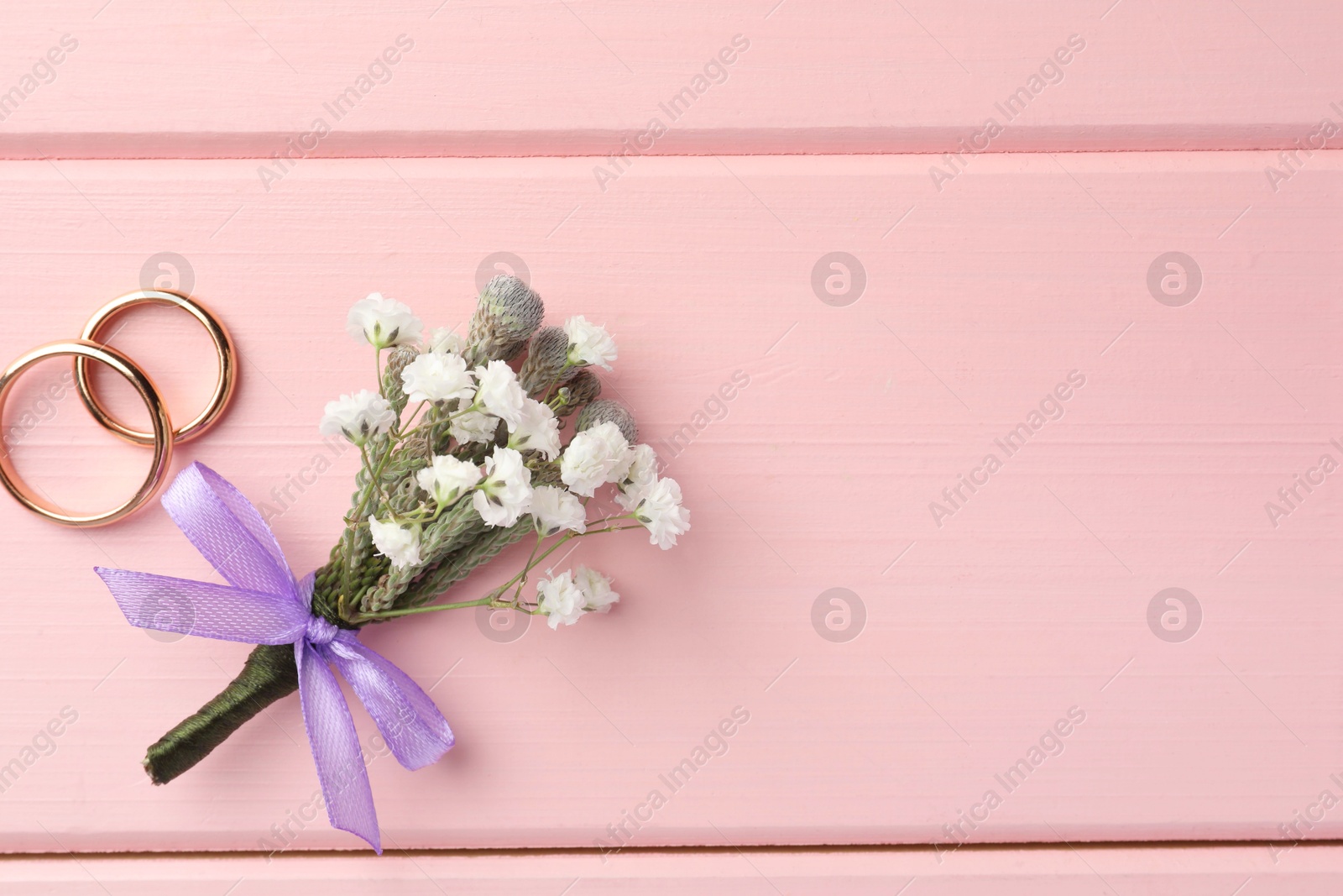 Photo of Small stylish boutonniere and rings on pink wooden table, flat lay. Space for text