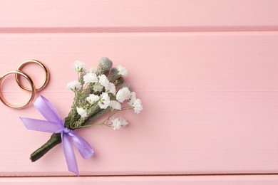 Small stylish boutonniere and rings on pink wooden table, flat lay. Space for text