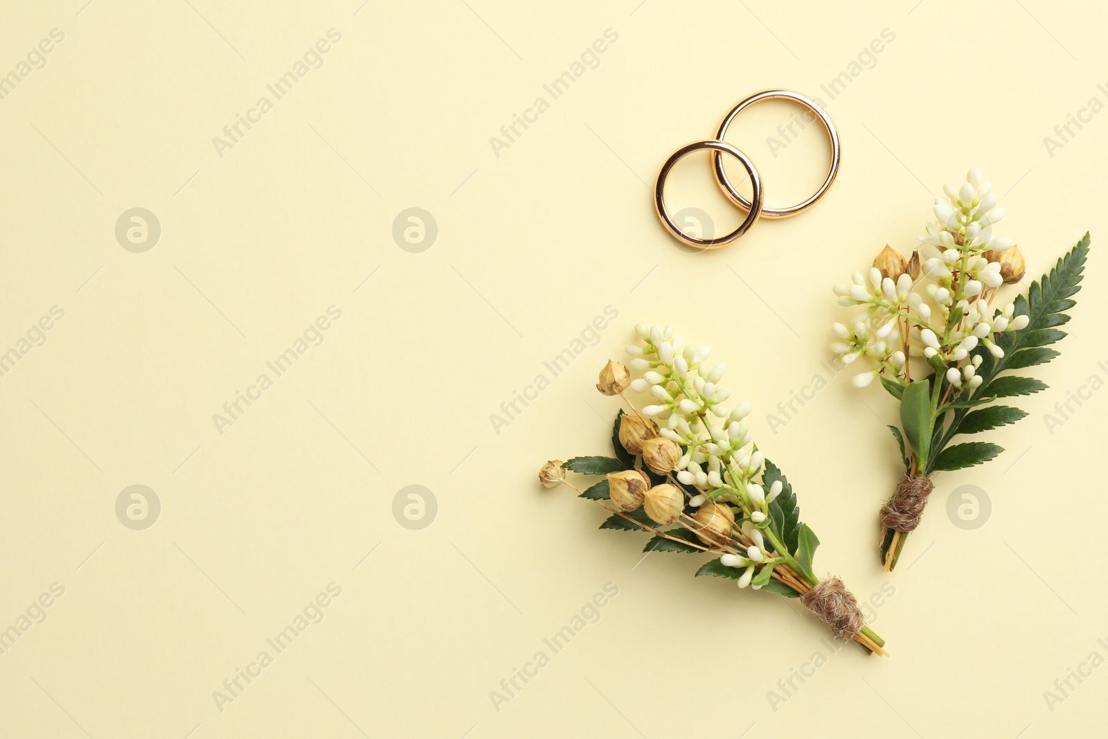 Photo of Small stylish boutonnieres and rings on beige background, flat lay. Space for text