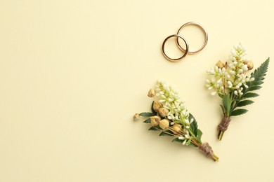 Small stylish boutonnieres and rings on beige background, flat lay. Space for text