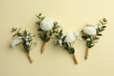 Many stylish boutonnieres on beige background, flat lay