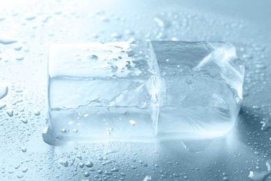 Piece of clear ice and water drops on light grey table