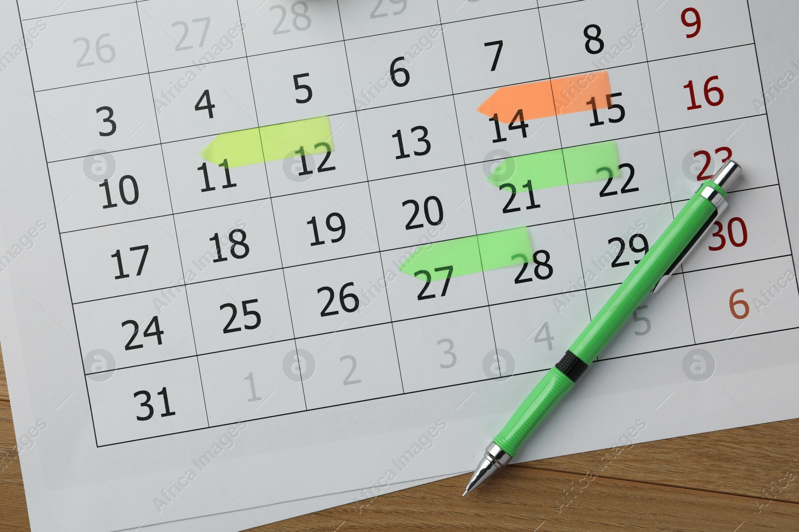 Photo of Timetable. Calendar page with marked dates and pen on wooden table, top view