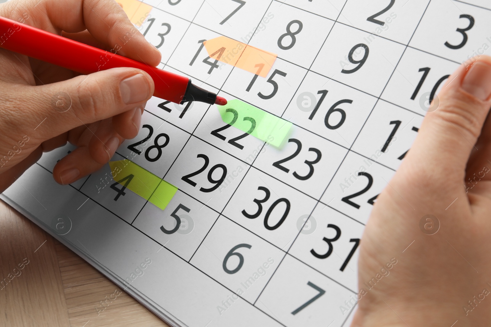 Photo of Timetable. Man marking date in calendar with felt pen at wooden table, closeup