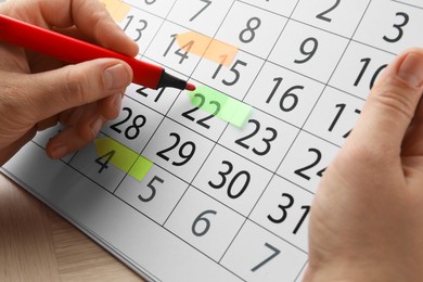 Photo of Timetable. Man marking date in calendar with felt pen at wooden table, closeup