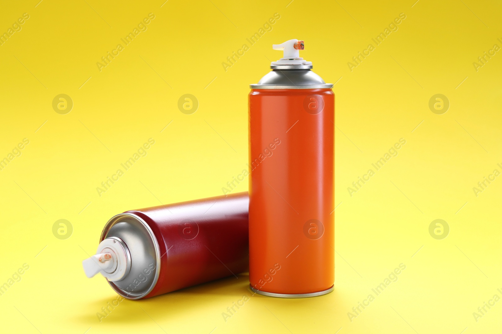 Photo of Two spray paint cans on yellow background