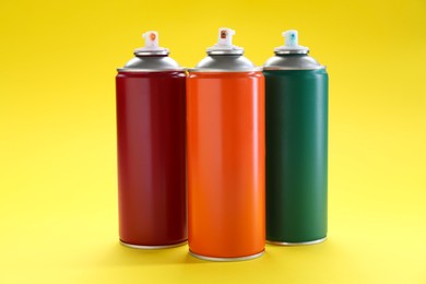 Three spray paint cans on yellow background