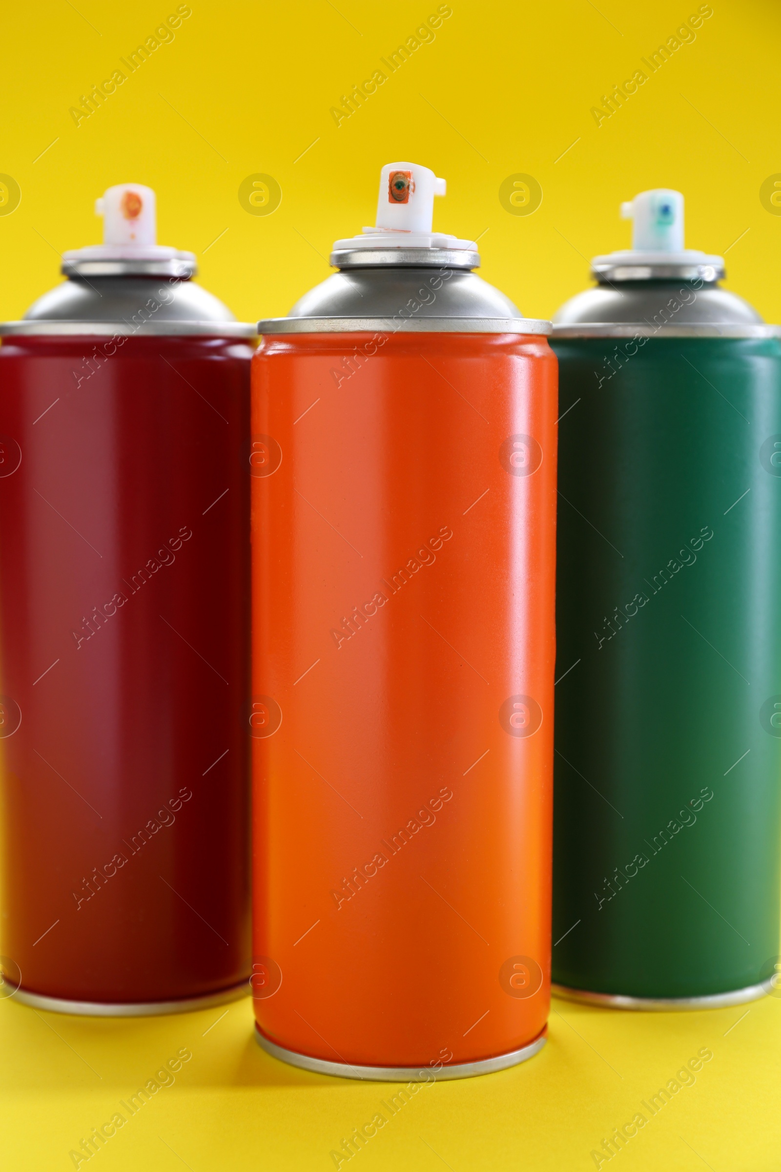 Photo of Three spray paint cans on yellow background