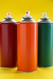 Three spray paint cans on yellow background