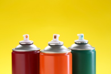 Photo of Three spray paint cans on yellow background, closeup. Space for text