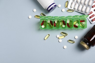 Photo of Different pills, organizer and medical jars on light background, flat lay. Space for text