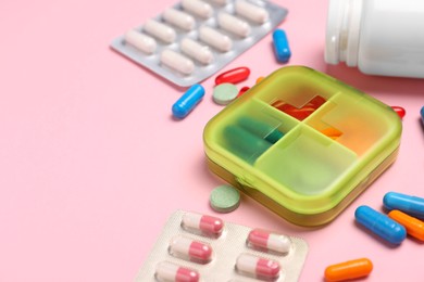 Photo of Different pills, organizer and medical jar on pink background, closeup. Space for text