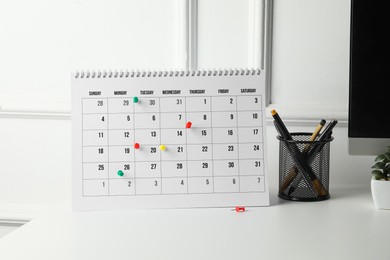 Photo of Timetable. Calendar with drawing pins and stationery on white table indoors