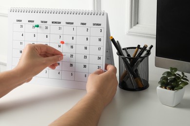 Photo of Timetable. Man marking date in calendar with drawing pins at white table, closeup