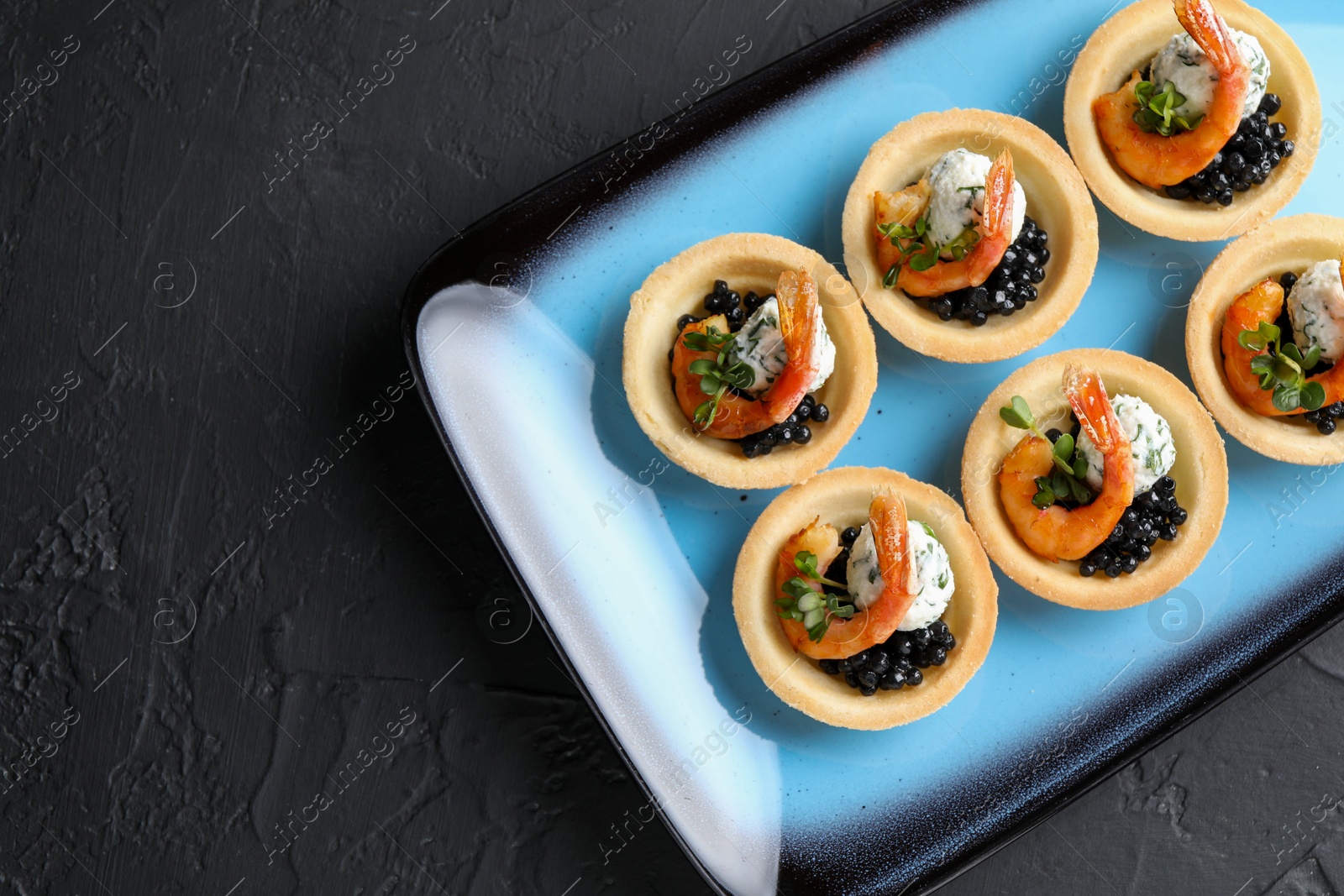 Photo of Delicious canapes with shrimps and black caviar on black textured table, top view. Space for text