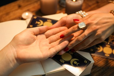 Photo of Fortune teller reading lines on woman's palm at wooden table, closeup. Chiromancy