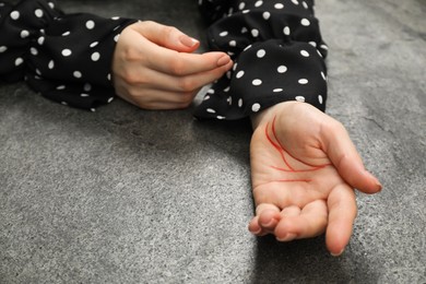 Woman showing palm with drawn lines at grey table, closeup. Chiromancy and foretelling