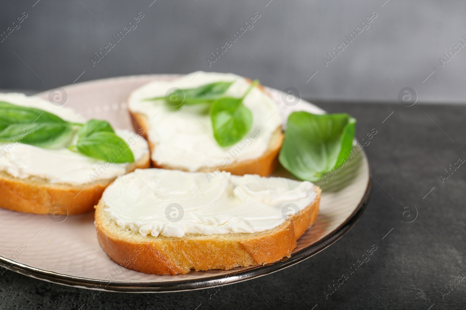 Photo of Delicious sandwiches with cream cheese and basil leaves on grey table, closeup