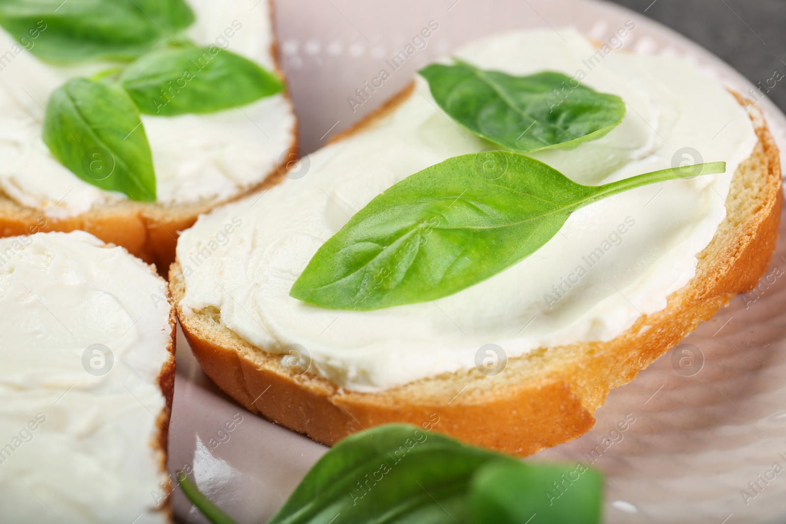 Photo of Delicious sandwiches with cream cheese and basil leaves on plate, closeup