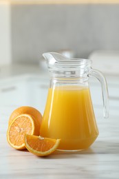 Photo of Tasty orange juice in jug and citrus fruits on white marble table