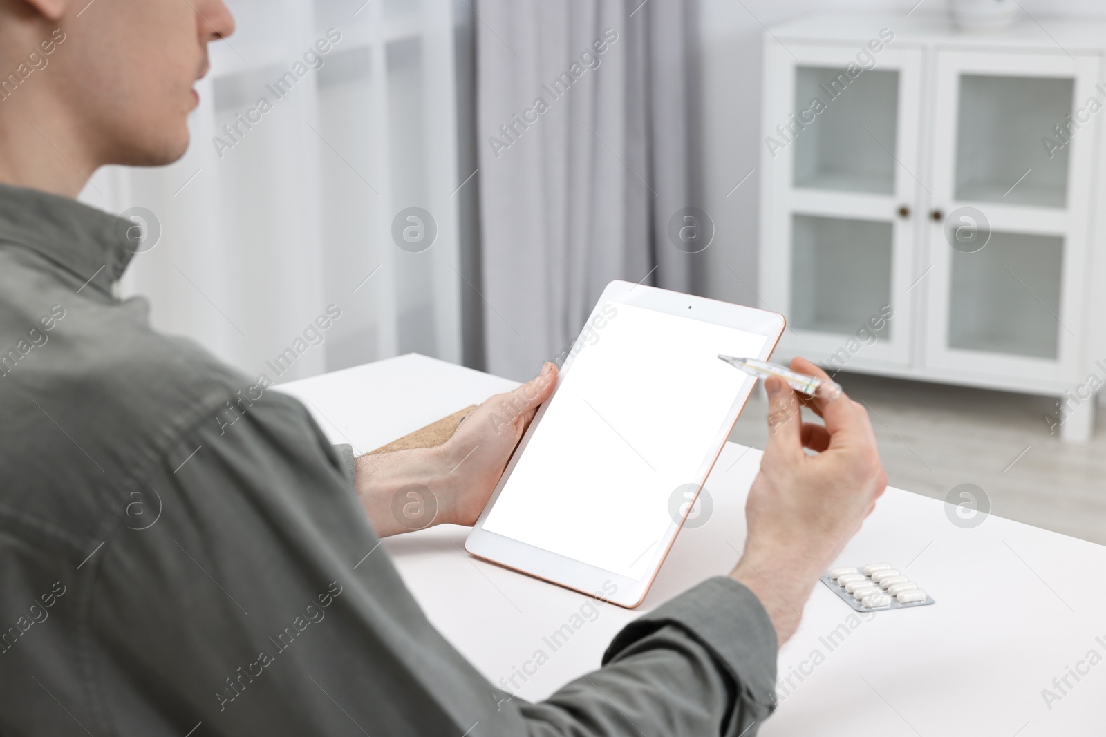 Photo of Sick man with thermometer having online consultation with doctor via tablet at home, closeup