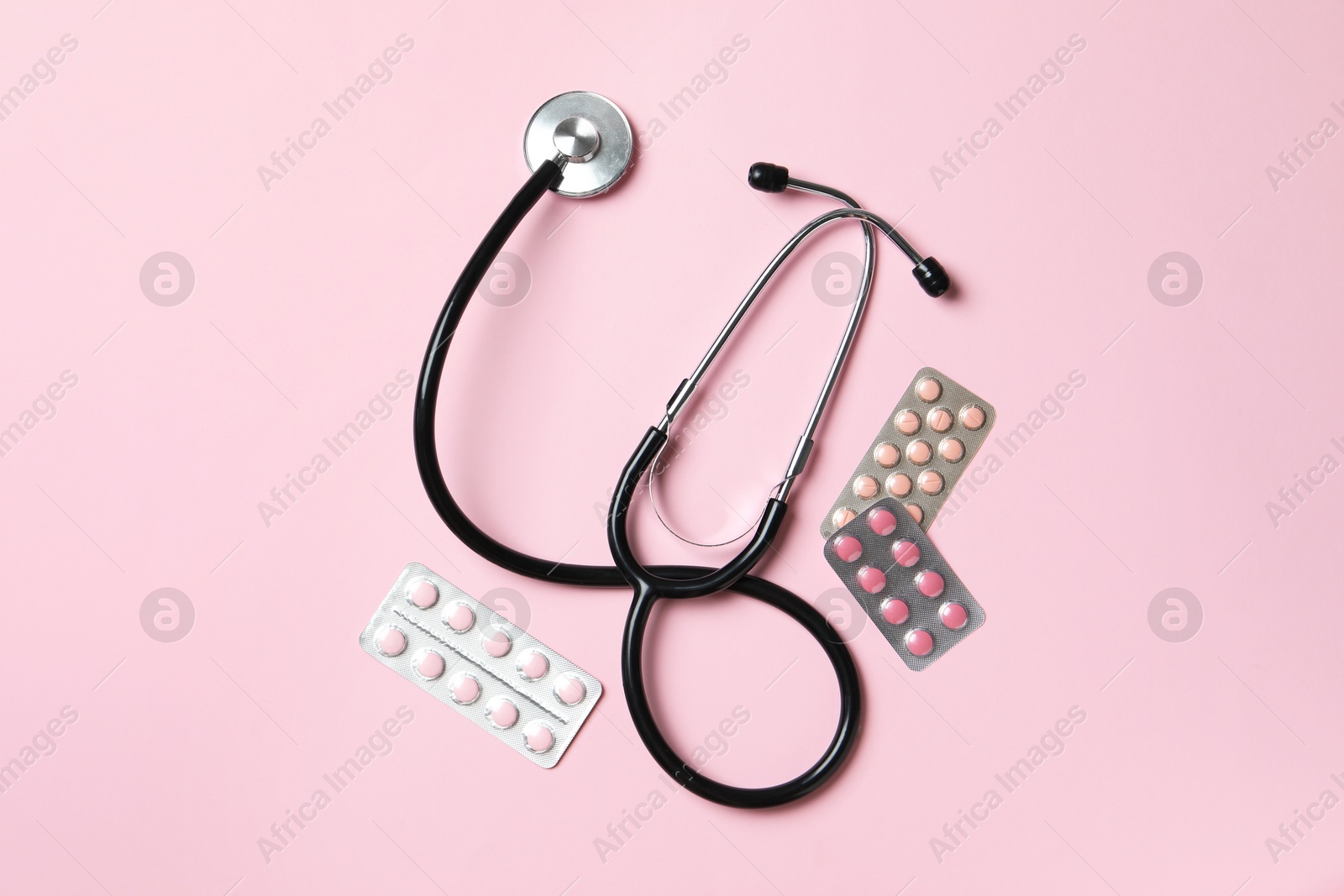 Photo of Stethoscope and pills on pink background, flat lay