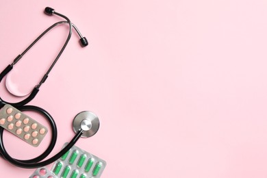 Photo of Stethoscope and pills on pink background, flat lay. Space for text