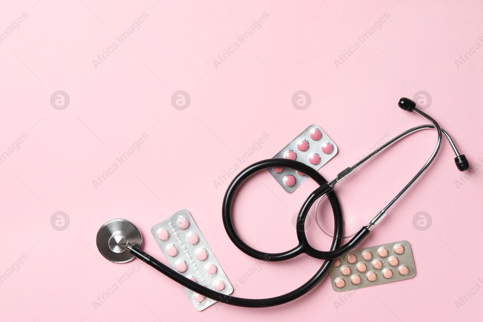 Photo of Stethoscope and pills on pink background, flat lay. Space for text