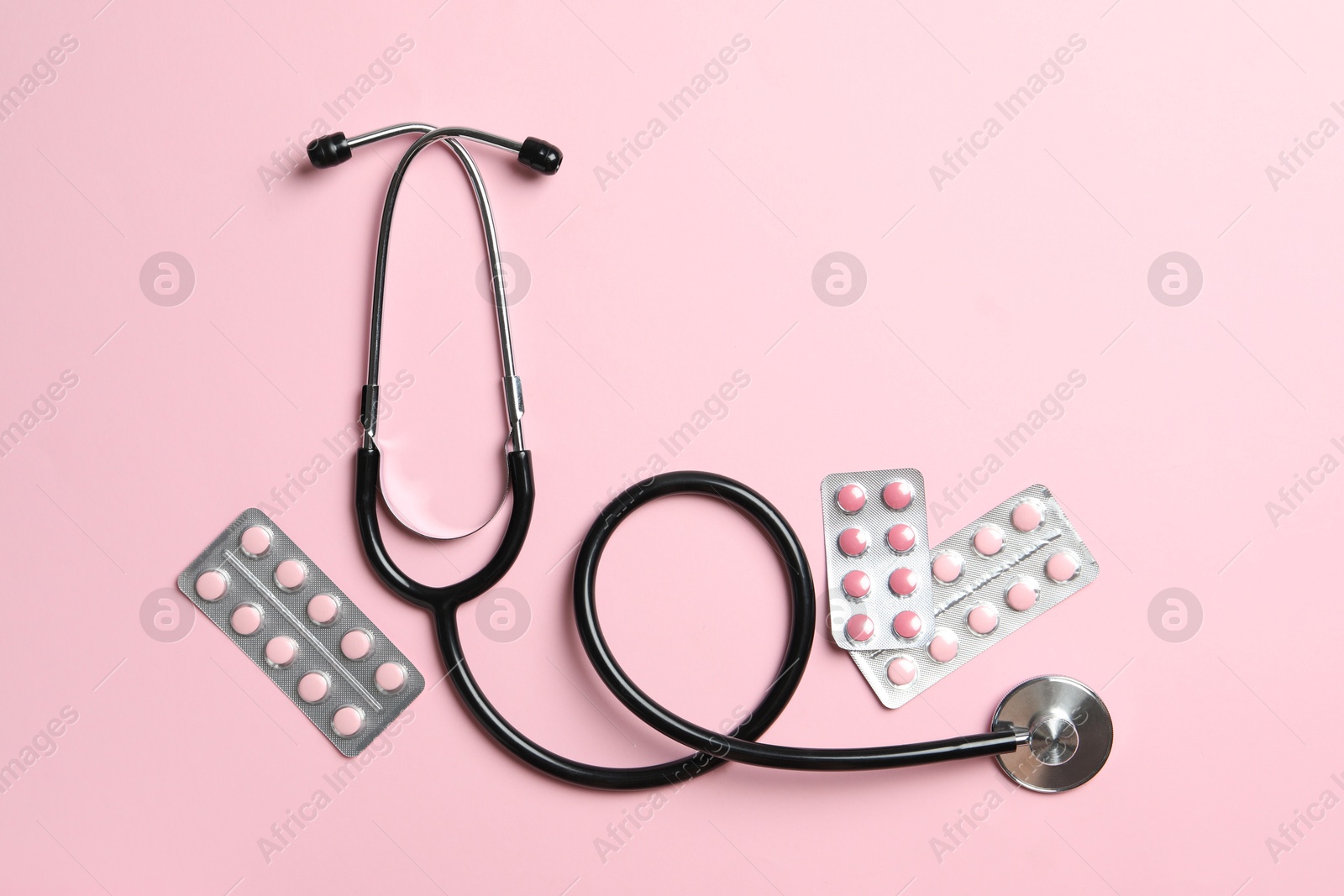 Photo of Stethoscope and pills on pink background, flat lay