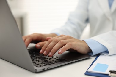 Photo of Doctor using laptop at white table in hospital, closeup