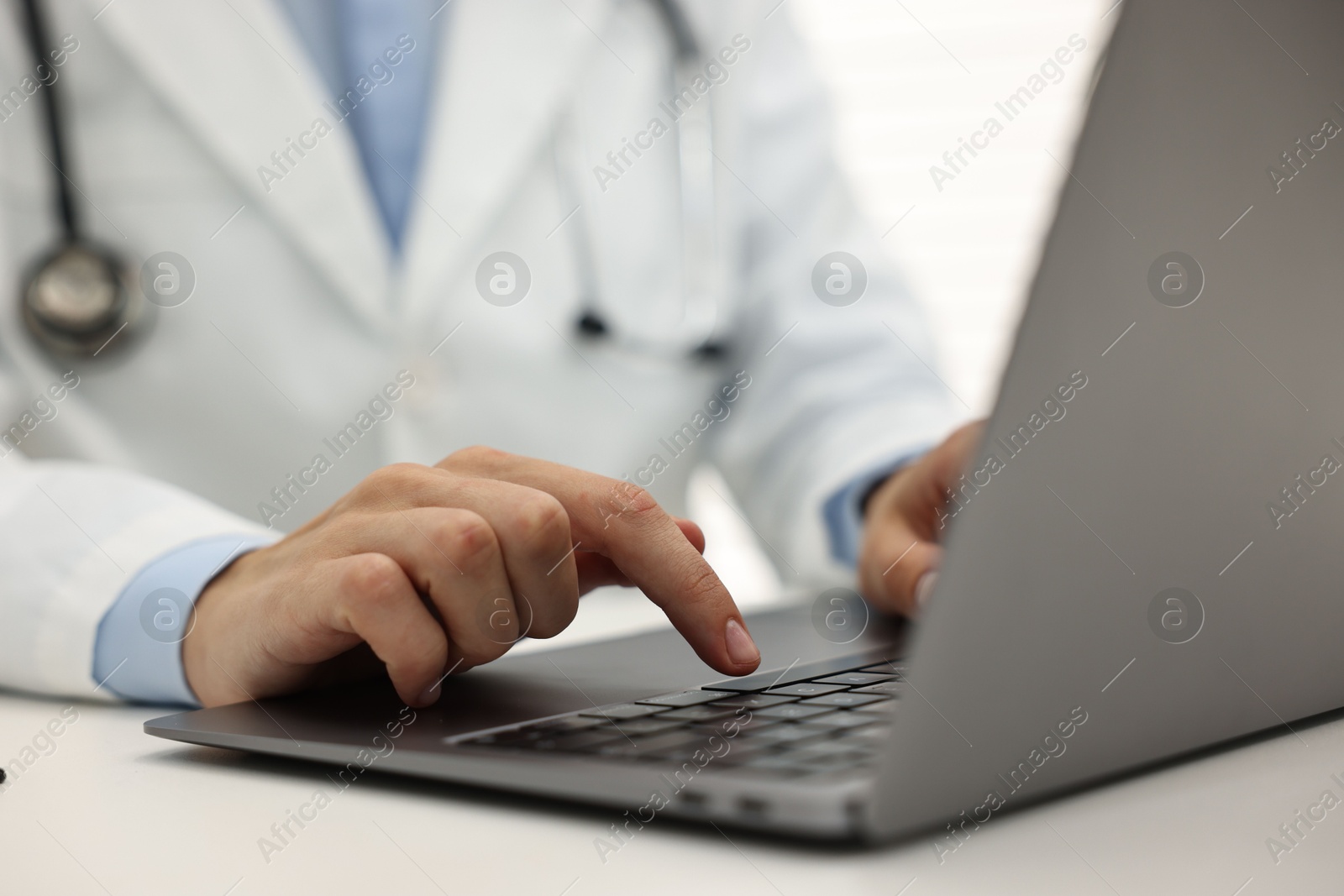 Photo of Doctor using laptop at white table in hospital, closeup