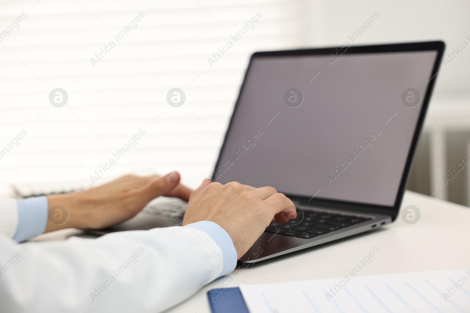 Photo of Doctor using laptop at white table in hospital, closeup