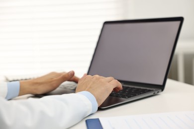 Photo of Doctor using laptop at white table in hospital, closeup