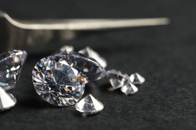 Photo of Many beautiful shiny diamonds and tweezers on black table, closeup. Space for text