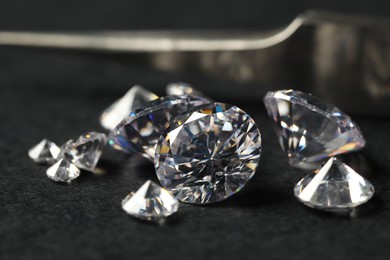 Photo of Many beautiful shiny diamonds and tweezers on black table, closeup