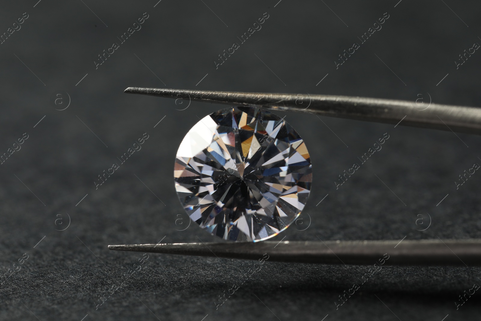 Photo of Beautiful shiny diamond and tweezers on black table, closeup