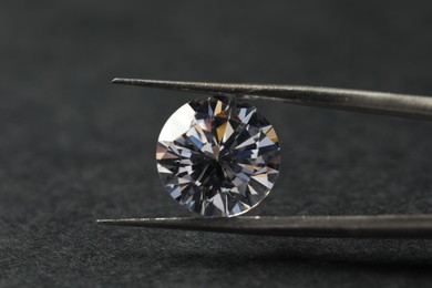 Photo of Beautiful shiny diamond and tweezers on black table, closeup