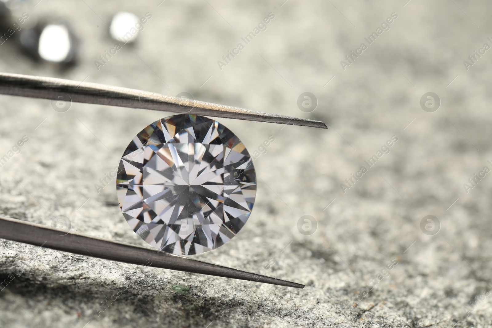 Photo of Beautiful shiny diamond and tweezers on grey textured table, closeup. Space for text