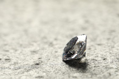 Beautiful shiny diamond on grey textured table, closeup. Space for text