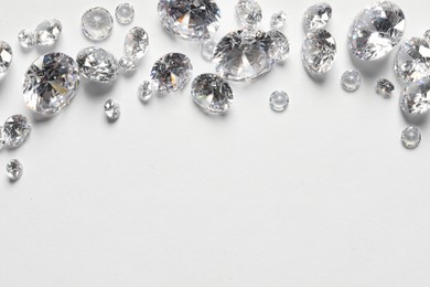 Many beautiful shiny diamonds on white background, flat lay. Space for text